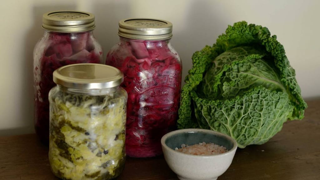 Three jars of fermented food, a cabbage and a small dish on a bench.